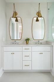 Two Antique Brass Swing Arm Pendants Illuminate Two Brass Mirrors Placed Over A White Dual Wash Brass Bathroom Lighting Bathroom Mirror Bathroom Light Fixtures