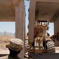 Equipment Operator Constructionman Kyle Holtzman directs Equipment Operator  Constructionman Eric Hofmans as he operates a wheel loader to move a stack  of lumber at the Ecole 5 Primary School.