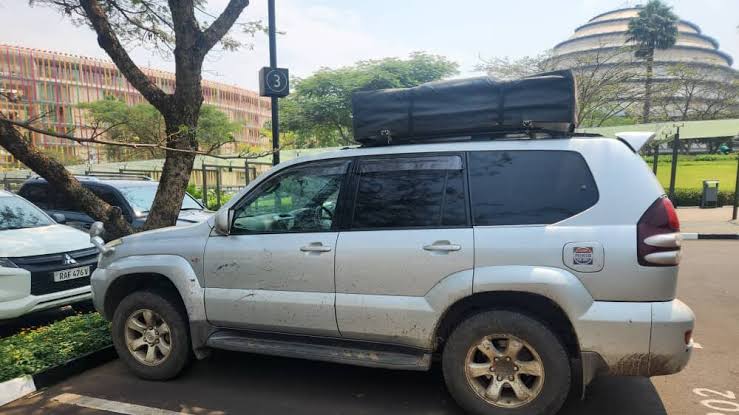 A silver Toyota Land Cruiser 4x4 equipped with an open rooftop tent parked in a scenic green valley at sunset during a 4x4 self drive Rwanda camping trip