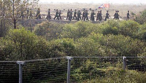 Mga resulta ng larawan para sa North Korean soldiers carrying the North Korean flag and shovels march Monday along a fenced border near the Chinese city of Dandong"