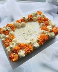 A rectangle cake featuring orange and white icing swirls, gold sprinkles, and a 'Happy Birthday' message.