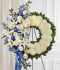 All white roses, daisies, lilies and more are accented with baby blue delphiniums and decorated with a light blue organza ribbon. Blue White Standing Wreath At From You Flowers