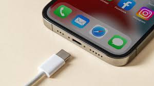 Smartphone iPhone sendo conectado a um carregador com cabo USB-C, mostrando o ícone de bateria carregando na tela.