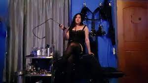 Dominatrice Mara dans une jupe en cuir, des jarretières, des bas et un  fouet BDSM Donjon POV - Darknesporn.com
