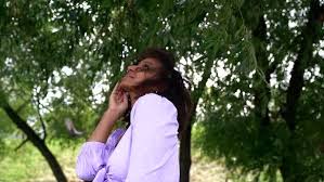 The puffiest of them all. A Young African Woman In A Lilac Top With Ties And Puffy Sleeves Poses Under Green Trees She Smiles By Yarmedia
