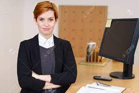 Confident Young Receptionist Behind The Front Desk In A Corporate Enterprise Or Hotel Standing With Folded Arms Looking At The Camera With A Quiet Thoughtful Smile Stock Photo Picture And Royalty Free