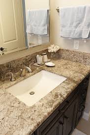A white and black sheepskin rug sits in front of a white flat front bath vanity fitted with an apron sink and a leathered black granite countertop fixed against a leathered black granite backsplash holding a wall mount faucet. 50 Best Granite Kitchen Bathroom Countertop Materials Ideas Bathroom Countertops Countertops Bathroom Countertop Materials