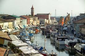 Lento canale urbano con capanni qua e là su palafitte e le case stan ritte tenendosi per mano. Porto Canale Cesenatico