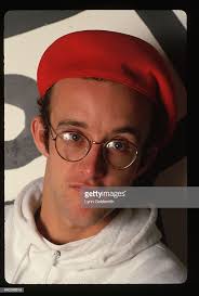 Close-up portrait of Keith Haring wearing red beret. He stands before...