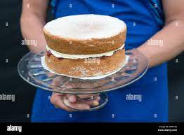 a glass cake stand held by person with traditional homemade victoria sponge  cake shallow depth of field Stock Photo - Alamy