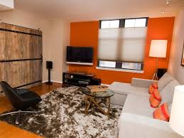 Orange and gray living room features a gray velvet sofa lined with orange pillows lined with a console table topped with orange lamps facing a brown suede tufted bench as coffee table. Orange Accent Wall Electrifies Contemporary Living Room Hgtv
