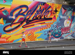 People walking past a mural painted by Queen Andrea entitled Believe on the  Bowery Mural Wall at the intersection of Bowery and Houston Street