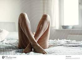 Eine Frau im Bett von der man nur nackte, lange, an den Fesseln überkreuzte  Frauenbeine sieht - ein lizenzfreies Stock Foto von Photocase
