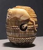 Netsuke definition in japanese art, a belt toggle (literally root for fastening), often carved ivory or wood, and traditionally used to secure a purse or small container suspended on a silk cord from the sash of a kimono, because most kimono were without pockets. Netsuke Wikipedia