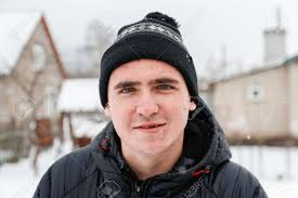Close-up Portrait Of Young Man In Warm Hat Outside On Rural Winter Snowy  House Background. Happy Millennial Smiling Outdoor, Cold Weather. Caucasian  Guy 20-25 Years. Face With Acne Or Herpes. Stock Photo,