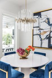 Deluxe dining room with a round dining table and purple velvet chairs that sit on a patterned area rug. Brass And Lucite Chandelier Over Round White Dining Table Contemporary Dining Room