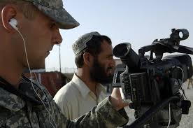 U.S. Army SGT. Brian Raley (left) from the 345th Mobile Public Affairs  Detachment (MPAD) checks the recording settings of his video camera as an  interpreter (center) stands by to translate, during an
