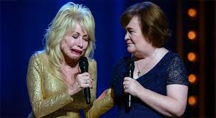 I still feel him beside me…” Dolly Parton broke down mid-performance as Susan  Boyle gently took her hand — a moment of quiet sisterhood that moved the  entire audience to tears. They