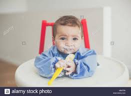 6 month old baby boy feeding himself yoghurt with a spoon