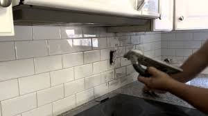 A black range hood is fixed to white staggered backsplash tiles accented with black grout. Grout Application On A Kitchen Backsplash Youtube