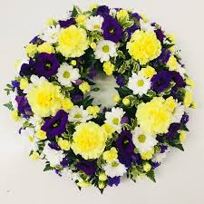 White casket covered with floral arrangements at a funeral service. Classic Wreath Purple White And Yellow Katherine S Florists