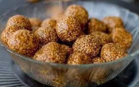 Tilgul Ladoo, sesame and jaggery balls, round and golden brown, served on a traditional plate