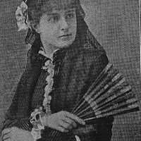 Portrett. To kvinner. En sitter på en stol, en sitter på knærne ved siden  av stolen. Kvinnene har på seg kjole eller skjørt og bluse.Bildet er tatt  på Reine i Lofoten. -