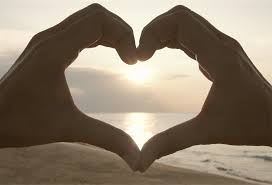 Hand in a heart shape in front of an ocean sunset