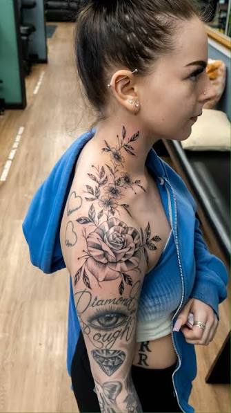 Witness the enchanting beauty of this floral tattoo that gracefully adorns the skin, starting from the shoulder and ascending to the upper neck. 🌹🌿 A large, striking rose blooms boldly on the ...