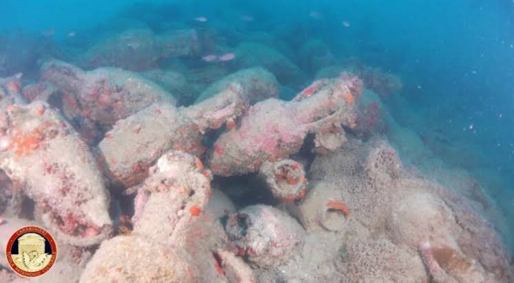 Underwater view of ancient Roman amphorae scattered across the seabed at a shipwreck site off the coast of Sicily.