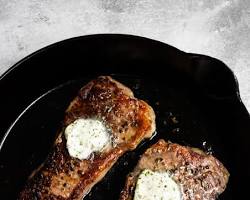 Image of New York strip steak searing on a cast iron skillet