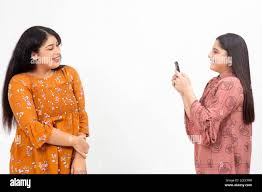 Two young Indian girls taking photo on their smart phone. Cute teenagers  having fun with each other on a white background Stock Photo - Alamy