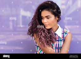 Portrait Of Charming Young Ethnic Young Woman With Curly Hair Tilting Head And Looking Away Against Colorful Glass Wall Stock Photo Alamy