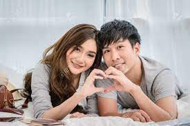 Closeup Happy Asian Lover Or Couple In Love With Doing Heart Form Hand  Action On The Bed In Bed Room At Modern Home, Boyfriend Pointing To The  Mobile Phone, Lover And Life