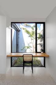 A brown cane chair sits at a white desk lit by a white desk lamp and positioned in a corner in front of a window. A Plank Of Wood In Front Of A Window Is An Easy Way To Make A Desk For A Home Office