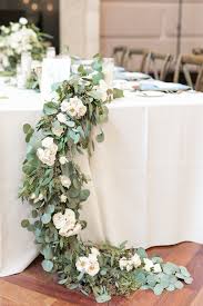 On The Wedding Reception Head Table Is A Lush Mixed Eucalyptus Garland Of Silv Wedding Reception Head Table Table Flower Arrangements Wedding Reception Flowers