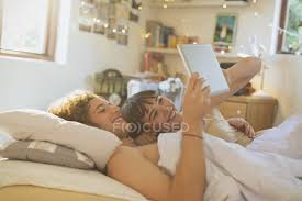 An elderly couple is both lying in bed one morning, having just woken from a good night's sleep. Smiling Young Couple Laying In Bed Using Digital Tablet Love Entertainment Stock Photo 199374982