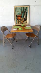 Bernard Buffet Lithograph Hangs Over A Vintage Hairpin Table And A Pair Of Folding Chairs From American Seati Folding Chair Mid Century Furniture Hairpin Table