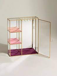 Jewelry hangs on hooks cleverly hidden behind a gold mirror hung above a cream rug on a wall adjacent to white recessed cabinets fixed above a white built in dresser finished with glass pulls. Gold Glass Pink Jewellery Cabinet Jewelry Cabinet Glass Shelves Decor Glass Shelves In Bathroom