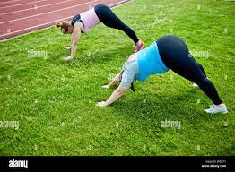 Two young active fat women bending over lawn with stretched arms and legs  during outdoor workout Stock Photo - Alamy