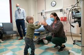 Hospital room: child and masked caregiver interacting by a bed, illustrating supportive care during transplant recovery