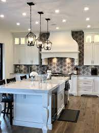 This updated contemporary kitchen features white walls, cabinets, and vent hood, dark marble countertops, hardwood floors, and a colorful spanish tile backsplash. White Kitchen With Patterned Cement Tile Backsplash Cement Tile Backsplash Mediterranean Kitchen Design White Kitchen