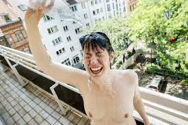 Nackte Frau auf dem Balkon duscht sich mit Wasser, lizenzfreies Stockfoto
