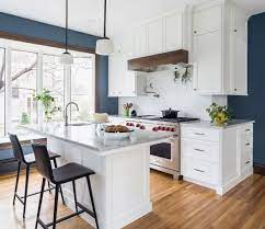 A Kitchen With Wood Flooring White Cabinetry Stainless Steel Appliances And A Blue Accent Wall Classic White Kitchen Blue Kitchen Walls Kitchen Remodel