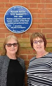 Jenny Spires and Rosemary Breen stand underneath Syd`s blue plaque.