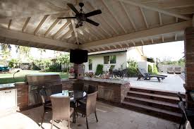An outdoor kitchen within a covered lanai in miami, florida features a cozy fireplace sitting area. Outdoor Amenities Azul Verde Design Group