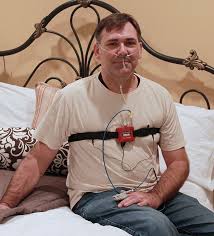 Man With Home Sleep Testing Device Sitting On A Bed Clayton Sleep Institute