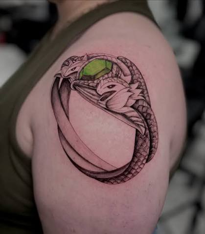 The Ring of Barahir is depicted as two intertwined serpents with emerald eyes, their heads meeting under a crown of golden flowers. One serpent upholds the crown, while the other devours it,