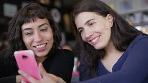 Two young women looking at smartphone device screen smiling. Female friends  s