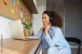 Smiling young african american teen girl wear headphones video calling on  laptop. Happy mixed race pretty woman student looking at computer screen  watching webinar or doing video chat by webcam. фотография Stock |